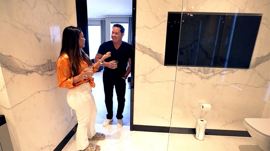 Dolores Catania and Paul Connell standing in their bathroom that has a large wall TV.