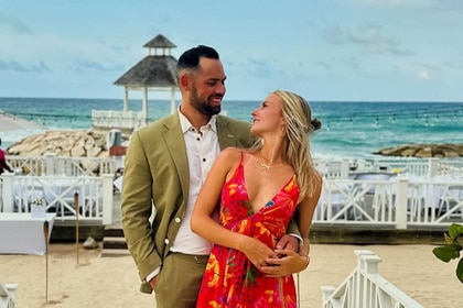 Taylor Ann Green and Gaston Rojas posing together in cocktail attire by a beach.