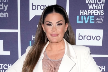 Brittany Cartwright wearing a fishnet top and a white blazer in front of the WWHL step and repeat.