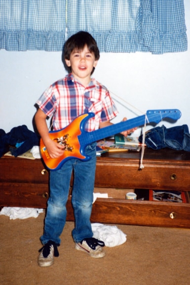 Tom Sandoval as a small child holding a guitar.