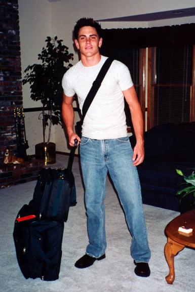 Tom Sandoval holds a suitcase while wearing a white t-shirt.