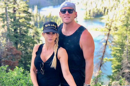 Alexis Bellino and Andy Bohn pose in a wooded area in athletic attire.