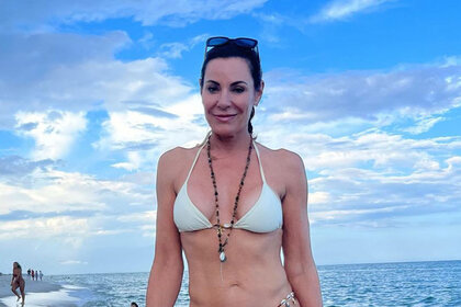 Luann De Lesseps in a white bikini on a beach.