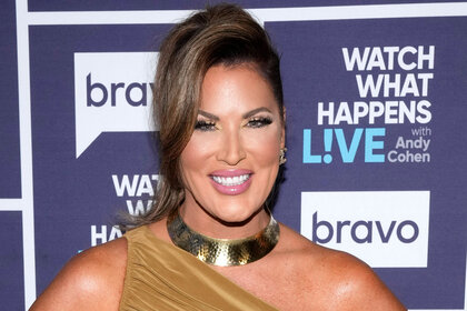 Emily Simpson smiling in an updo, gold choker, and one-shoulder, gold, mini dress at WWHL.
