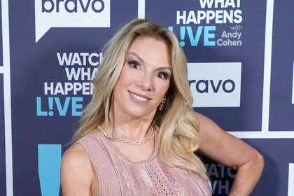 Ramona Singer in front of the WWHL step and repeat wearing a pink dress.