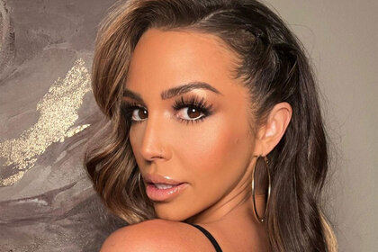 Scheana Shay in full glam in front of a marble artwork wearing a black top.