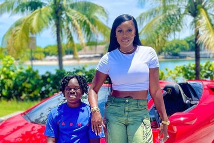 Wendy Osefo and her son Karter Osefo in front of palm trees and a red sports car together.