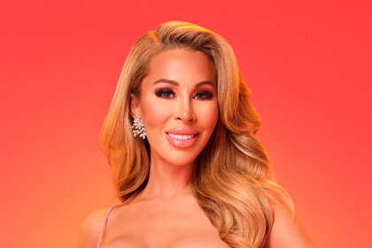 Lisa Hochstein smiling in a pink bustier and skirt set in front of a red and orange background.