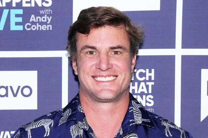 Shep Rose smiling in a navy, zebra patterned, shirt in front of the WWHL step and repeat in New York City.