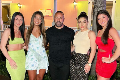 Joe Giudice posing with his daughters in front of a coral colored building.