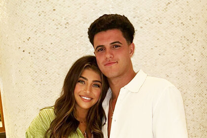 Gia Giudice and Christian Carmichael smiling and posing together in front of a tile column.