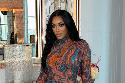Porsha Williams wearing a sheer, marbled designed, dress in front of decor.