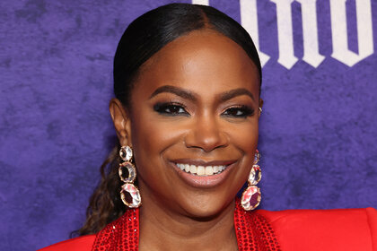 Kandi Burruss smiling in front of a step and repeat.