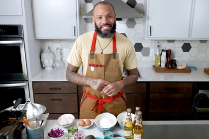Chef Justin Sutherland in an apron with a spread of ingredients