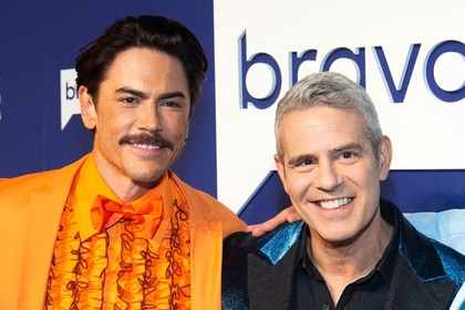 Andy Cohen and Tom Sandoval smiling together in front of a step and repeat at BravoCon 2022.