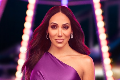 Melissa Gorga wearing a purple gown in front of a carnival backdrop.