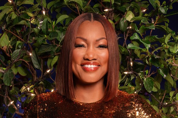 Garcelle Beauvais wearing a gold, sequins, gown in front of a Beverly Hills inspired set.