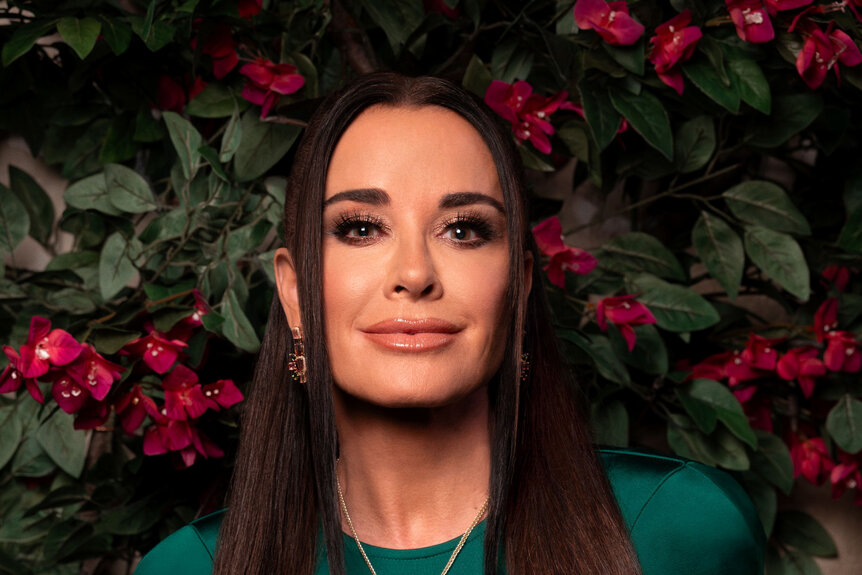 Kyle Richards wearing a silk, green, gown in front of a Beverly Hills inspired set.
