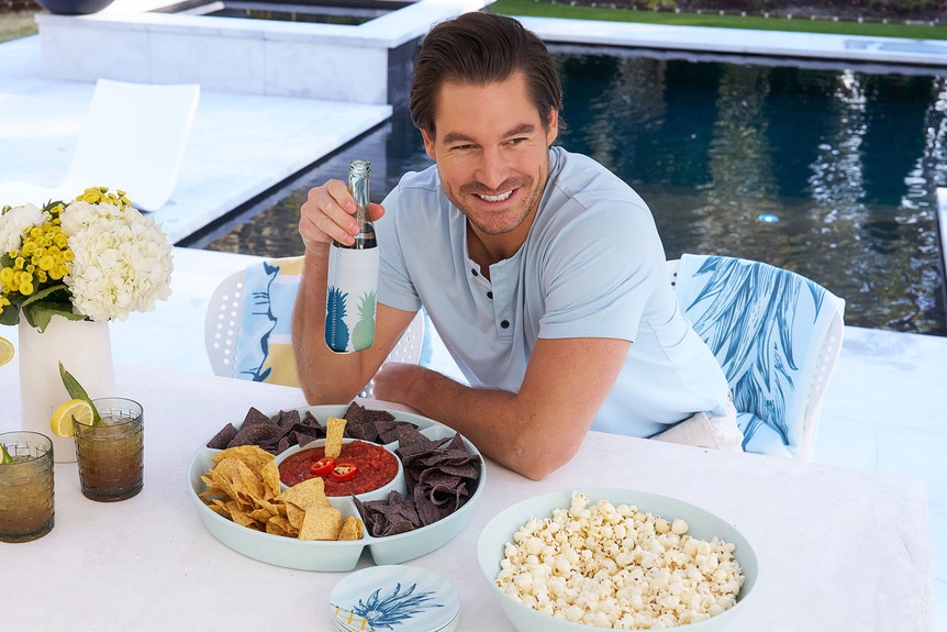 Craig Conover smiling in front of his pool at a table with food and drinks.
