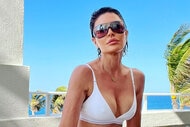 Lisa in a white bikini and sunglasses by a beach.