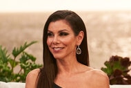 Heather Dubrow sitting and smiling in a black gown in front of a sunset.