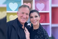 Heather Dubrow and Terry Dubrow smile together while in front of an heart display.