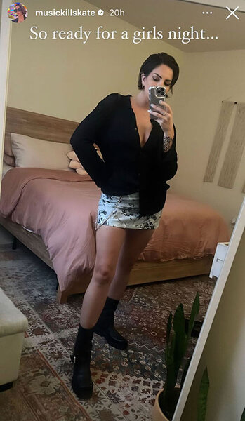 Katie in a mirror selfie wearing a black, long sleeve, top, a mini skirt, and black boots.