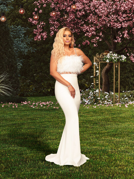 Robyn Dixon wearing a white feather crop top and a floor length skirt in a garden.