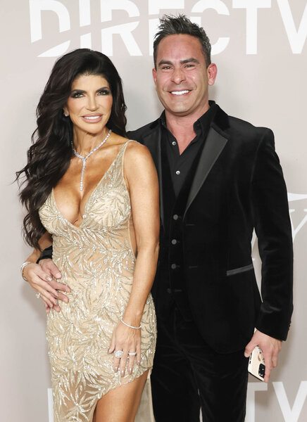Teresa Giudice posing in a sheer, crystal-embellished, v-cut gown with Louie Ruelas in front of a step and repeat.