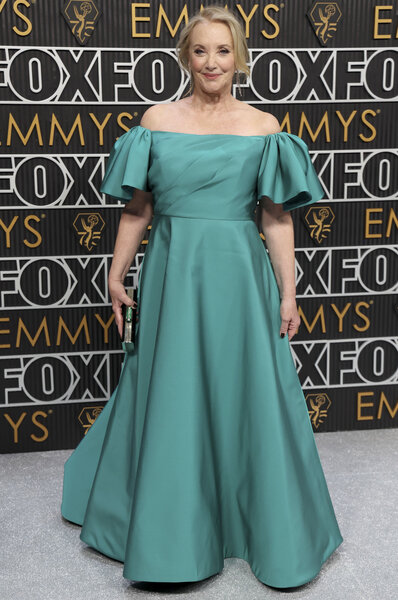 J. Smith-Cameron in a green, off-shoulder, gown posing in front of the Emmys step and repeat.
