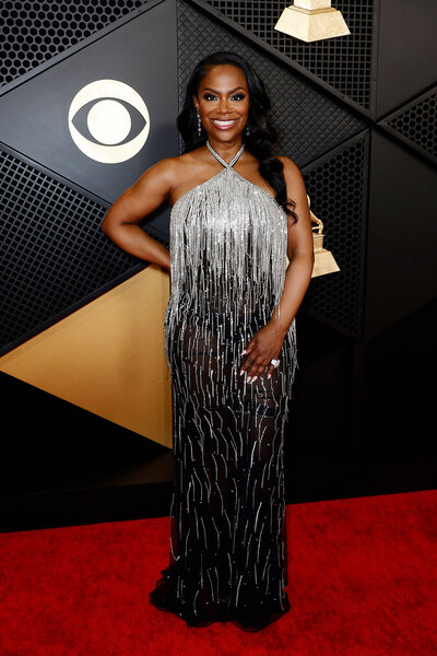 Kandi Burruss smiling in front of a step and repeat at the Grammys in a crystal embellished gown.