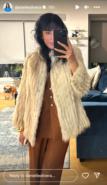 Danielle Olivera in front of a mirror wearing a fur coat and brown outfit.