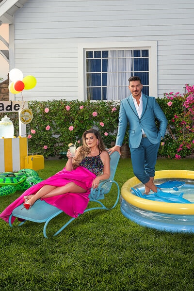 Jax Taylor wearing a blue suite and Britanny Cartwright wearing. a black and pink gown on a lawn with a baby pool