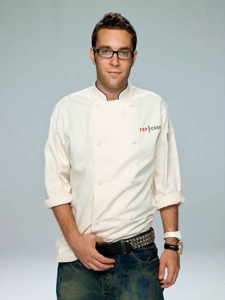 Ilan Hall wearing his chef's jacket and jeans in front of a grey backdrop