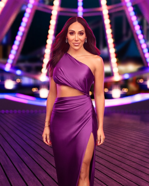 Melissa Gorga wearing a purple gown in front of a carnival backdrop.
