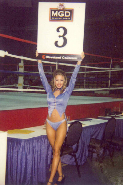 Lisa Hochstein smiling with a large sign in front of a boxing ring.