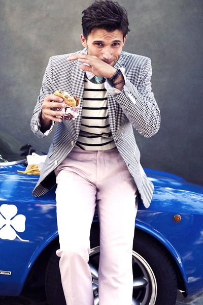 Tom Schwartz posing with a sandwich in front of a blue car.