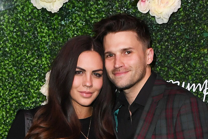 Katie Maloney and Tom Schwartz in front of a floral step and repeat at an event.