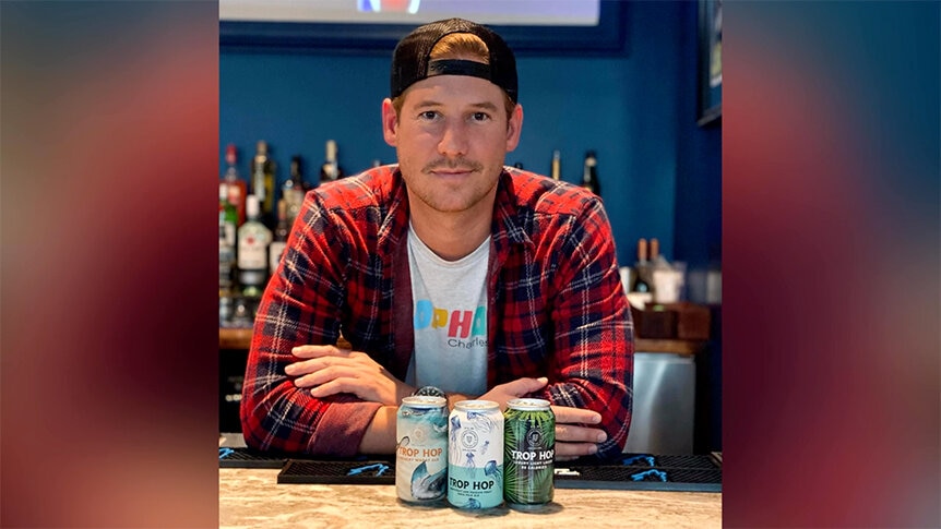 Austen Kroll in a plaid shirt posing with beer cans from his company.