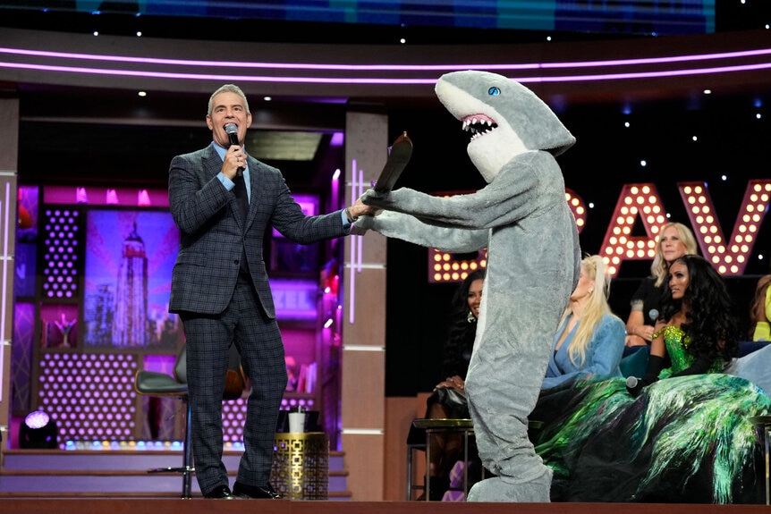 Andy Cohen, and Anderson Cooper in costume as a shark, on stage during a taping of WWHL at Bravocon 2022.