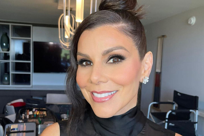 Heather Dubrow smiling with full glam and a top bun in an all black outfit.