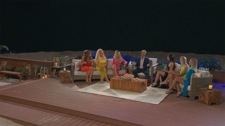 Andy Cohen and the RHOC cast sit on the reunion stage in front of a black background.