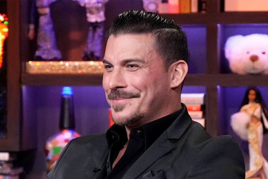 Jax Taylor smiling in an all black suit while sitting in the WWHL clubhouse.