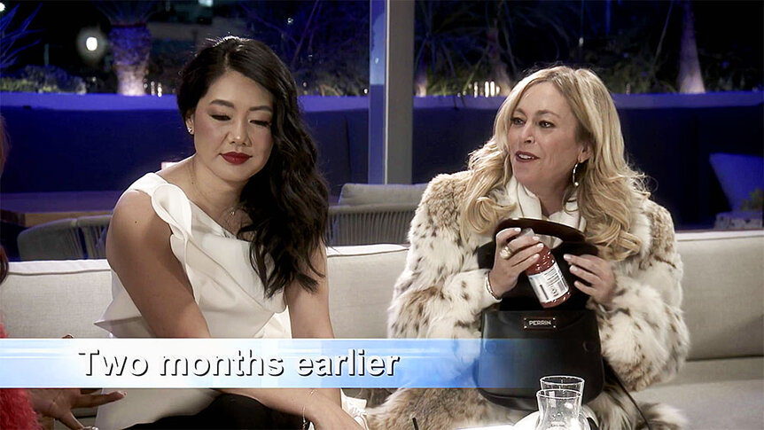 Sutton Stracke holding a bottle of grapefruit juice from her purse while sitting next to Crystal Kung-Minkoff.