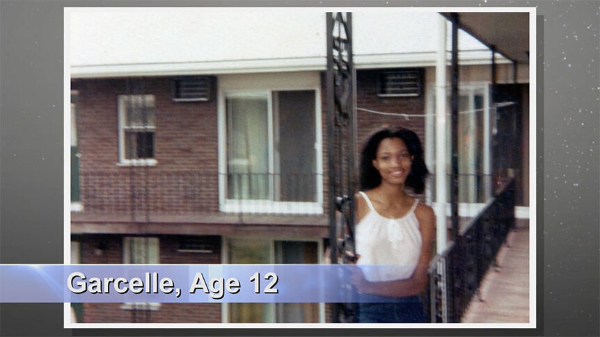 Garcelle Beauvais at 12 years old smiling while standing in an outdoor walkway.