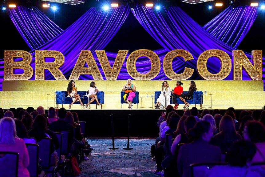 Members from the Viva Las Atlanta Peaches panel on stage with a "BravoCon" sign in the background during BravoCon 2023.