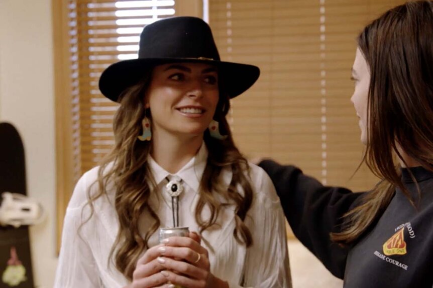 Katie Flood appears in a cowboy hat and bolo tie on Winter House Season 3 Episode 5.