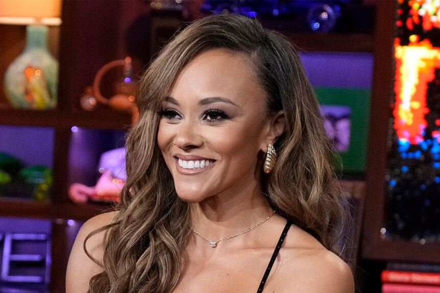 Ashley Darby smiling in a black, v-cut, dress at the Watch What Happens Live clubhouse.