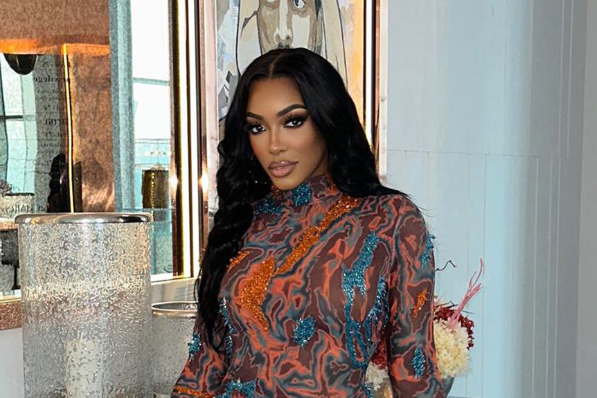 Porsha Williams wearing a sheer, marbled designed, dress in front of decor.