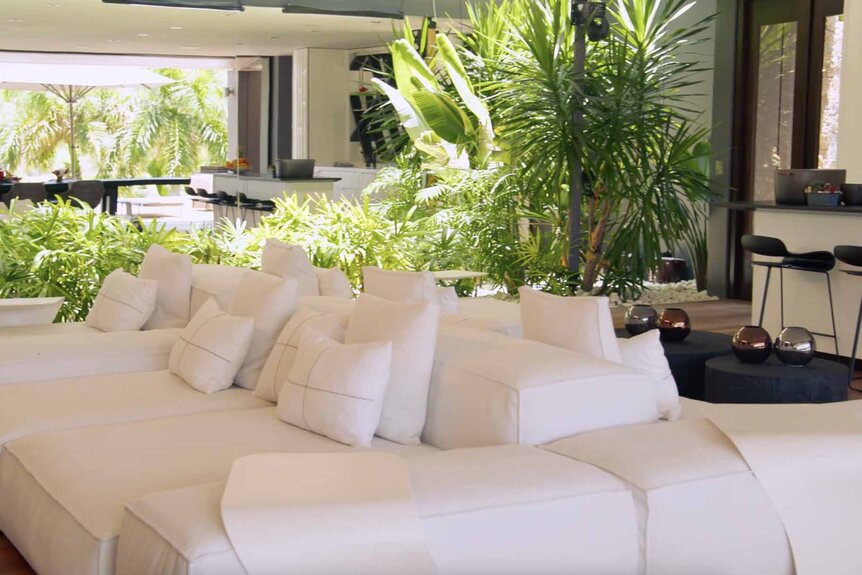 A living room with a large white couch and large plants furniture.
